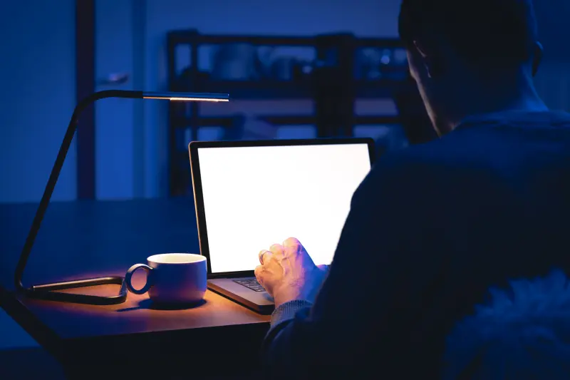 Travail tardif sur ordinateur portable, dans un bureau plongé dans le noir.