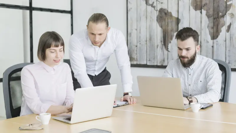 Un formateur accompagne deux participants sur leurs ordinateurs.